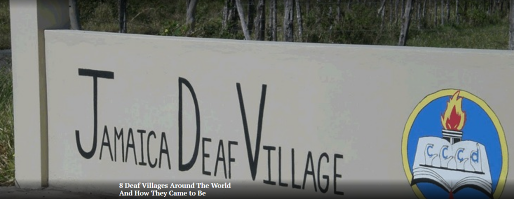 Entrance sign saying 'Jamaica Deaf Village' with 'CCCD' on a book inside a blue circle