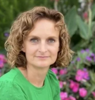 Nancy Letts, blond/brown hair, white skin with a green shirt.  Flowers in the background.