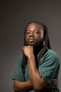 Franklin Jones, Jr, a black man with braided hair and black beard wearing a green shirt from boston university